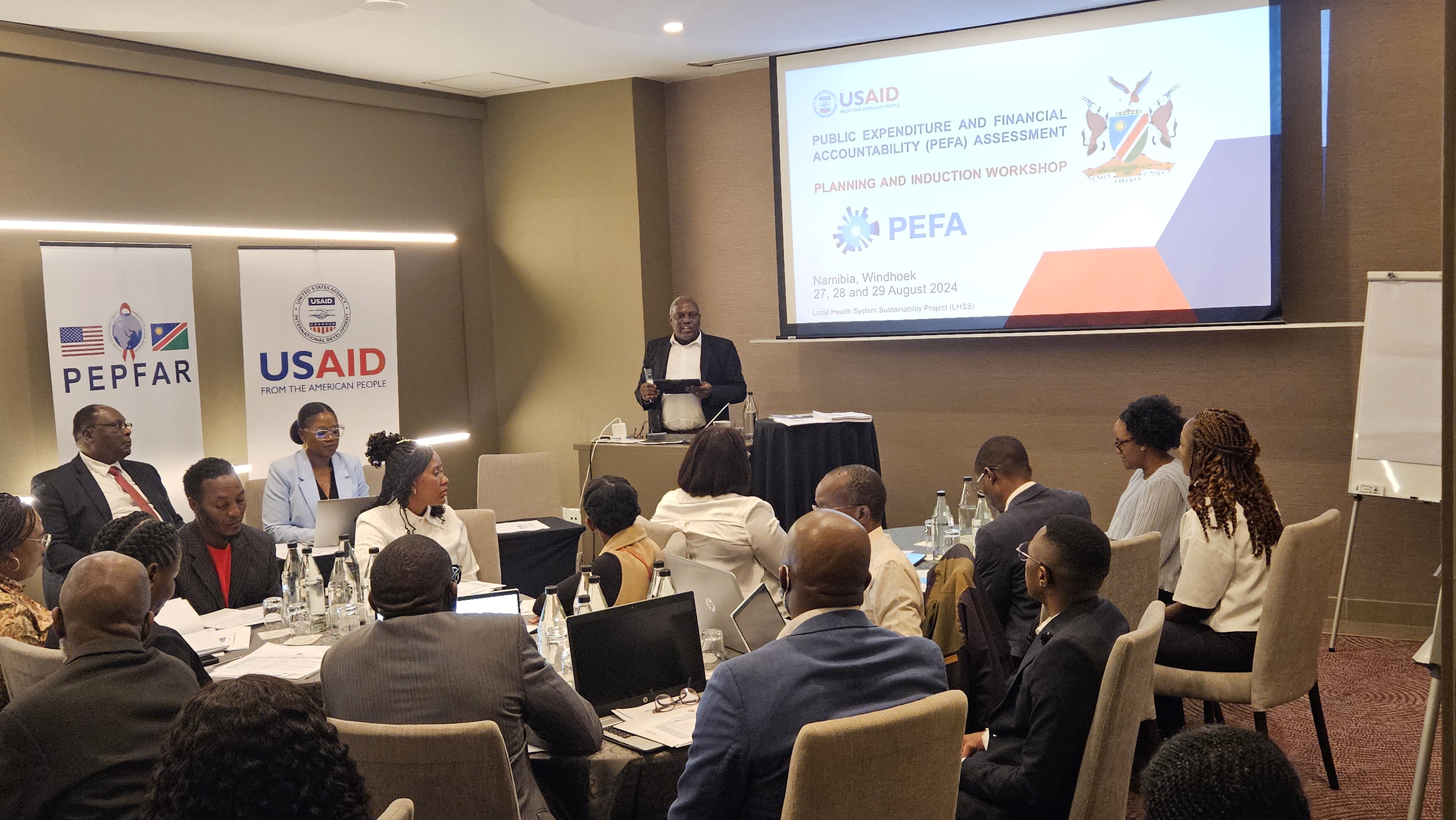 A meeting including ministries of health and other stakeholders. There is a a picture of the USAID logo in the background.