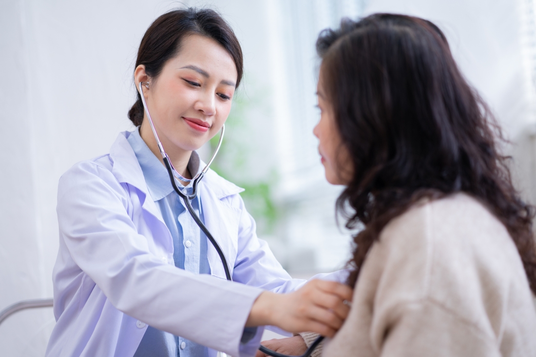 A female doctor uses a stethoscope to listen to a female patient's heart and lungs.